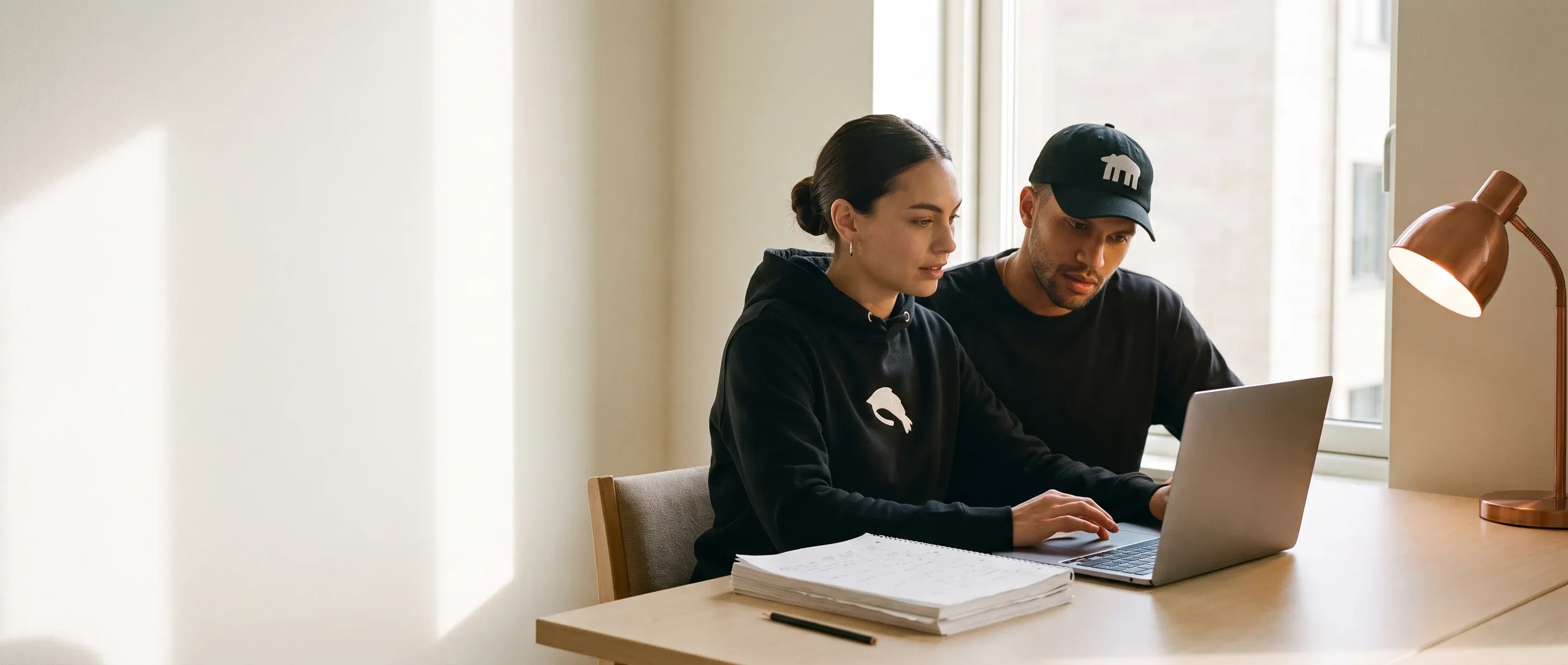 A woman shows a sceptical man something on her laptop, a stack of paper with handwritten notes beside them