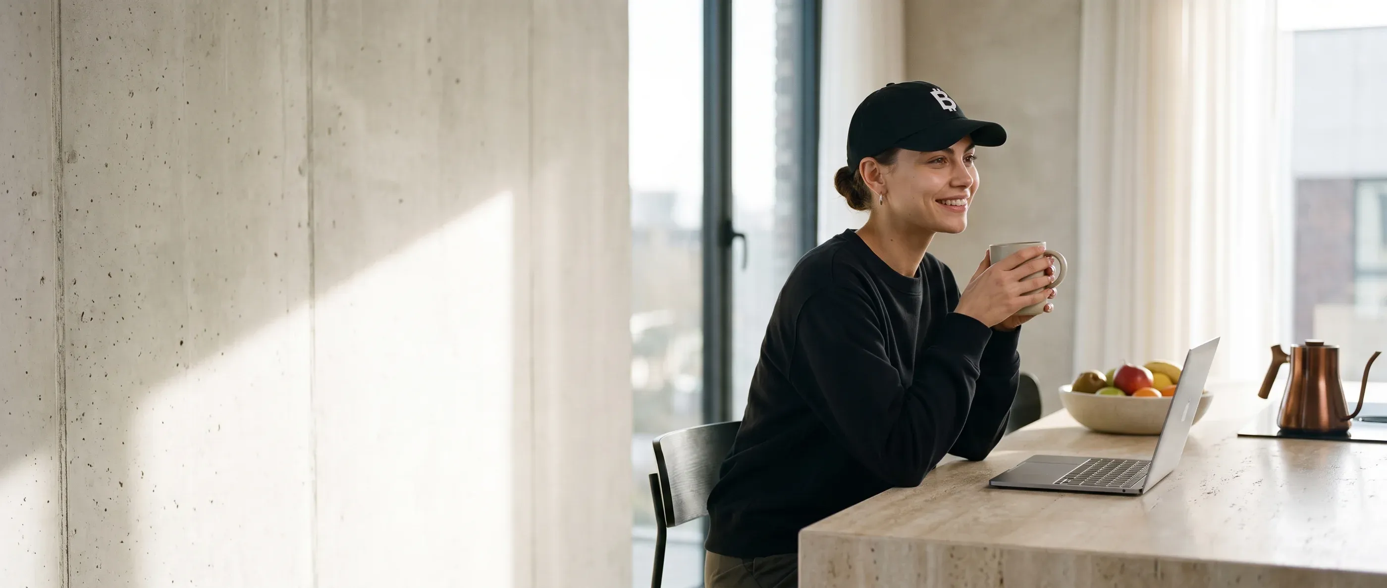 A person in a black whale hoodie at a plain concrete desk in morning light, an empty notebook in front