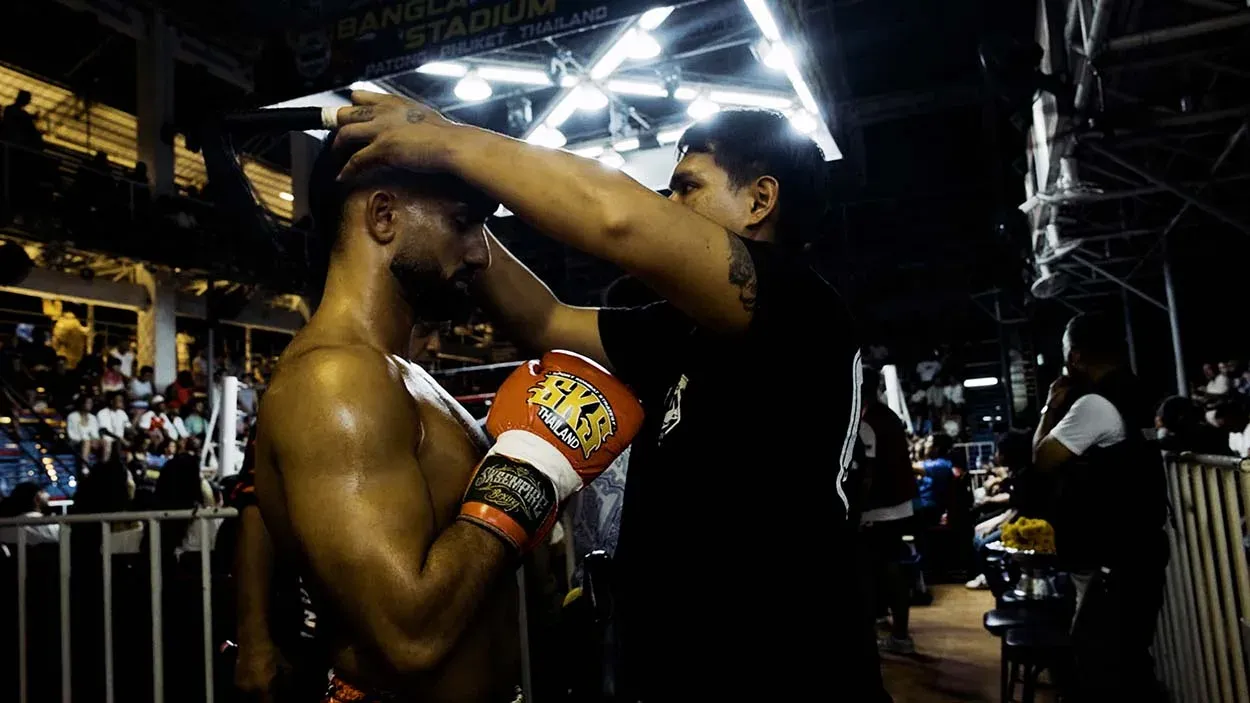 Thai coach handing fighter Aarian Asgari his headgear, Phuket Boxing Stadium